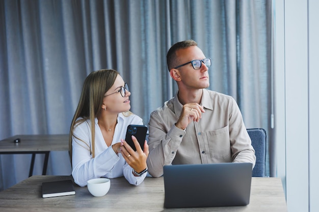 Fröhliche geschäftsleute, die einen laptop in einem büro verwenden glücklich lächelnde junge unternehmer bei der zusammenarbeit in einem modernen arbeitsbereich zwei junge geschäftsleute, die zusammen an einem tisch sitzen