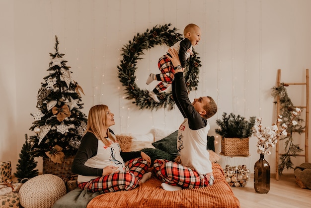 Fröhliche glückliche Familie im Schlafanzug mit einem Kind, das auf dem Bett im Schlafzimmer küsst. Neujahr Familienkleidung sieht Outfits. Valentinstag Feier Geschenke