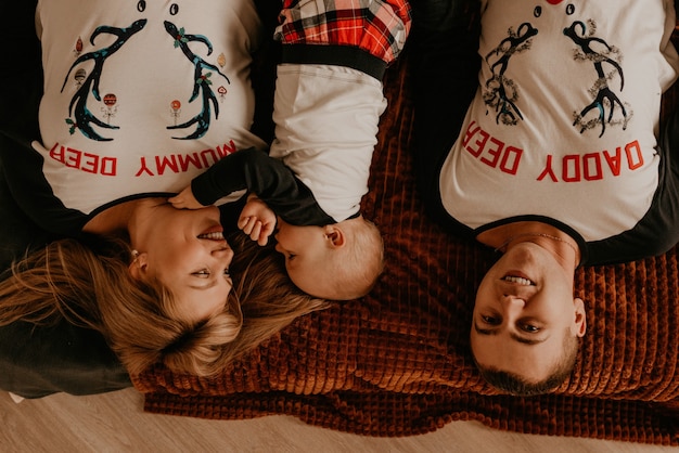 Fröhliche glückliche Familie im Schlafanzug mit Kind liegen auf dem Bett im Schlafzimmer. Neujahr Familienkleidung sieht Outfits. Valentinstag Feier Geschenke