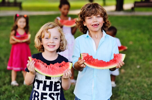 Fröhliche glückliche Kinder essen an einem sonnigen Sommertag eine reife Wassermelone im Park auf dem Rasen