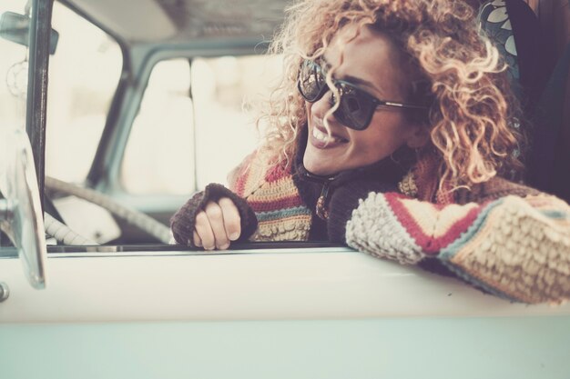 Fröhliche, glückliche, schöne kaukasische junge Frau, die aus dem Fenster eines alten Vintage-Van-Busses mit Sonnenbrille schaut und lächelt