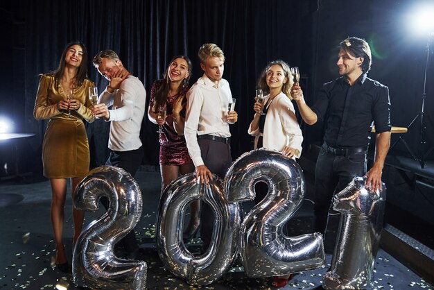 Fröhliche Gruppe von Menschen mit Getränken und Luftballons in den Händen, die das neue 2021-Jahr feiern.