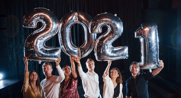 Fröhliche Gruppe von Menschen mit Getränken und Luftballons in den Händen, die das neue 2021-Jahr feiern.