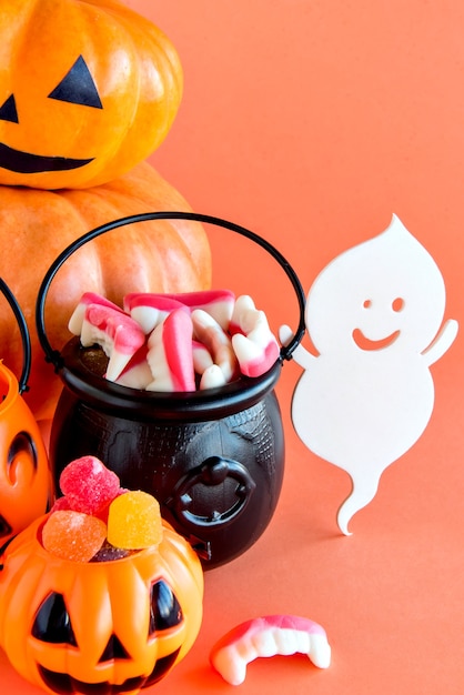 Fröhliche Halloween-Dekoration. Kürbis, Kessel, Schädel und gummiartige Bonbons auf orangem Hintergrund.