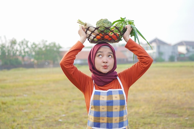 Fröhliche Hijab-Frau hebt einen Gemüsekorb über den Kopf