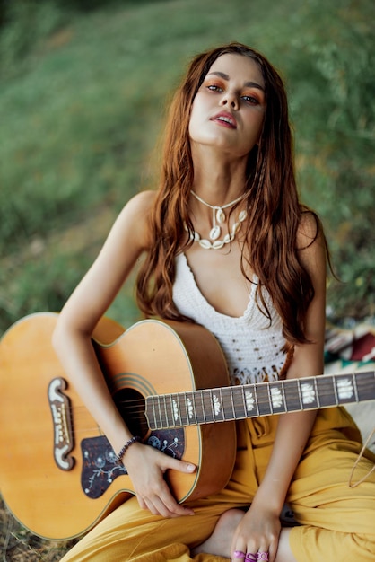 Fröhliche Hippie-Frau mit Gitarre lächelt in der Natur am See sitzend
