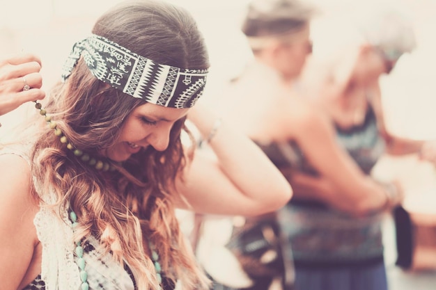 Fröhliche Hippie-Kleidung und Accessoires im indischen Stil, junge Dame legte eine Halskette an und genieße die Freizeitbeschäftigung mit Freunden im Hintergrund, Vintage-Filter und helles Bild