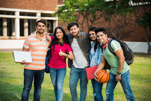 Fröhliche indische asiatische junge Gruppe von College-Studenten oder Freunden, die zusammen lachen, während sie auf dem Campus sitzen, stehen oder gehen