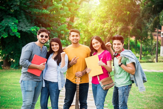 Fröhliche indische asiatische junge Gruppe von College-Studenten oder Freunden, die zusammen lachen, während sie auf dem Campus sitzen, stehen oder gehen