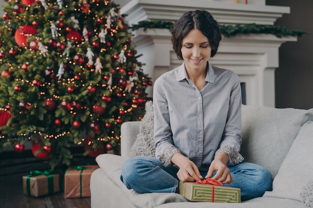 Fröhliche italienische Frau, die sich zu Hause auf Weihnachten vorbereitet, Weihnachtsgeschenk einpacken und verpacken