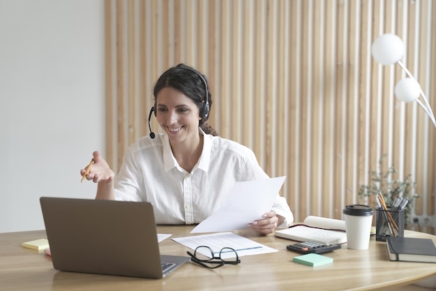 Fröhliche italienische Tutorin im Headset führt Online-Webinar auf Laptop im modernen Heimbüro durch