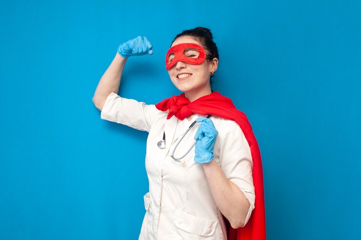 Fröhliche junge Ärztin in Uniform im Superman-Kostüm auf blauem Hintergrund, Krankenschwester-Superheldin