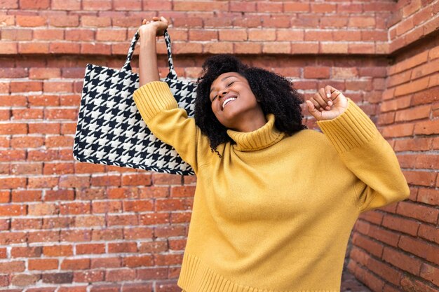 Fröhliche junge afrikanisch-amerikanische Frau tanzt mit ihrer Handtasche Glücks- und Lifestyle-Konzept
