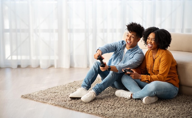 Fröhliche junge afroamerikanische Frau und Mann spielen ein Computerspiel mit einem Joystick