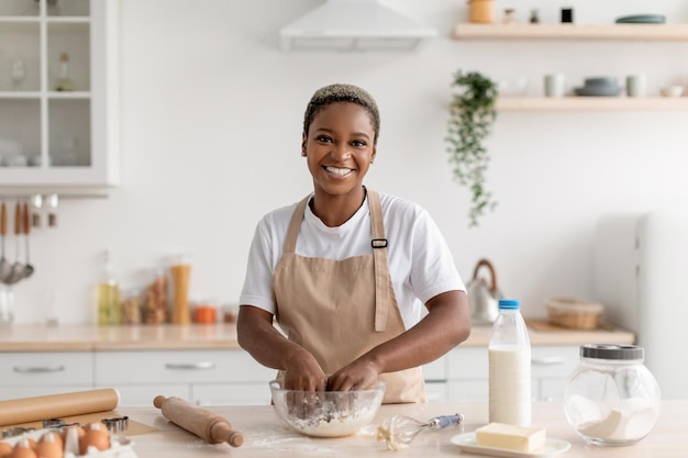 Fröhliche junge afroamerikanische Köchin Bloggerin in Schürze macht Kuchenteig