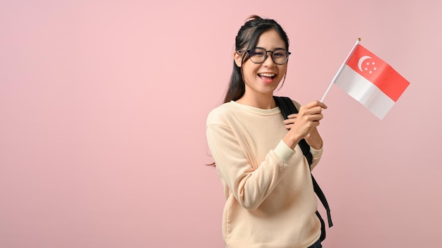 Fröhliche junge asiatische Frau, die eine Singapur-Flagge auf rosa isoliertem Hintergrund zeigt