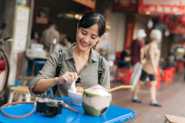 Fröhliche junge asiatische Frau mit Rucksackreisenden, die Streetfood auf dem Streetfood-Markt in China Town in Bangkok Thailand genießen