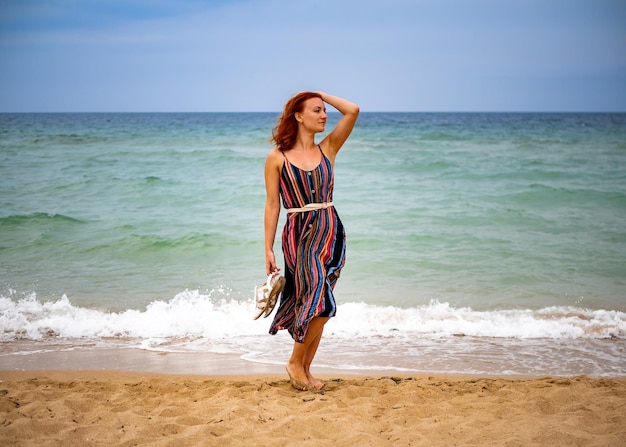 Fröhliche junge Boho-Frau, die an einem sonnigen, warmen Tag auf einer tropischen Insel in den Meereswellen spazieren geht und Spaß hat