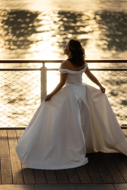 Fröhliche junge Brautfrau im weißen Kleid läuft, Sommerschießen in der Nähe eines Wassers. Hochzeit