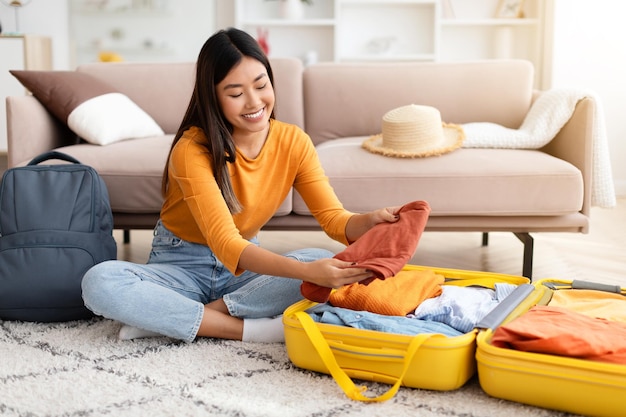 Fröhliche junge Chinesin packt zu Hause Koffer