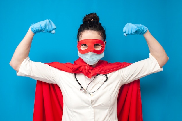 Foto fröhliche junge doktorin in uniform in superman-kostüm auf blauem hintergrund weibliche krankenschwester superheldin