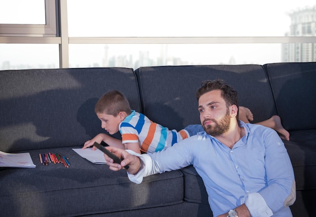 Fröhliche junge Familie, die zu Hause mit einem Tablet und einem Zeichenset für Kinder zusammen auf dem Sofa spielt