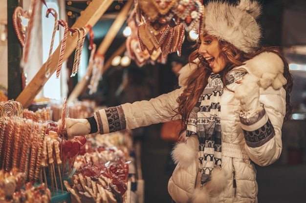 Fröhliche junge Frau amüsiert sich in der Neujahrsnacht auf einem Weihnachtsmarkt in der Stadtstraße.