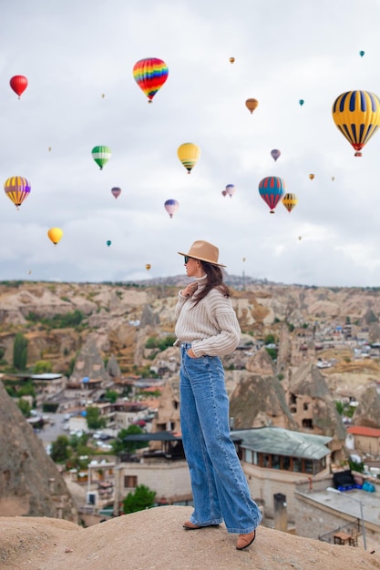 Fröhliche junge Frau bei Sonnenaufgang, die Heißluftballons in der Türkei in Kappadokien beobachtet