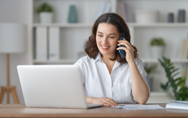 Fröhliche junge Frau, die arbeitet und Webinar-Podcasts auf Laptops ansieht, die sich aus der Ferne unterhalten