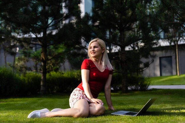 Fröhliche junge Frau, die auf ihrem Laptop im Freien im Park im Internet surft