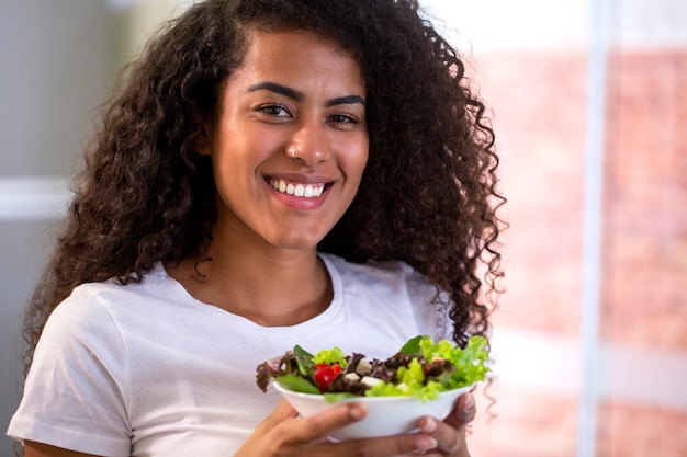 fröhliche junge Frau, die Gemüsesalat in der Hauptküche isst.