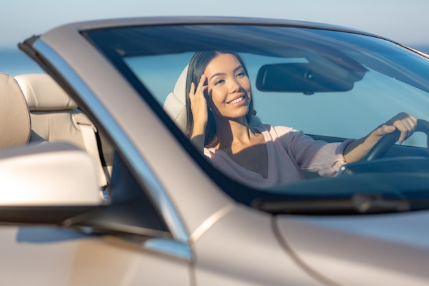 Fröhliche junge Frau, die im Cabrio sitzt und in den Spiegel schaut