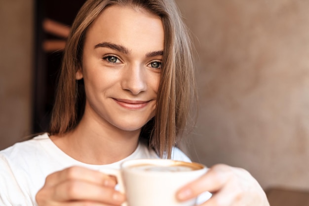 fröhliche junge Frau, die Kaffee trinkt und lächelt, während sie in einem gemütlichen Café sitzt?