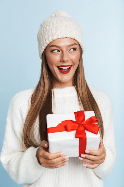 Fröhliche junge Frau, die Pullover und Hut trägt und Geschenkbox hält