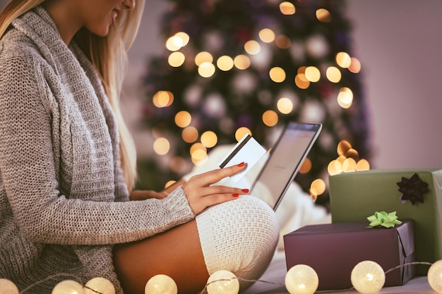 Fröhliche junge Frau, die sich zu Hause entspannt und Weihnachtsgeschenke online auf dem Laptop kauft.