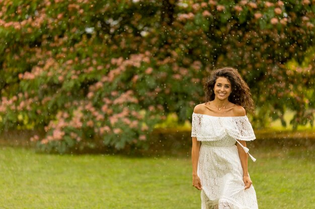 Fröhliche junge Frau, die vom Sommerregen im Park gefangen wurde