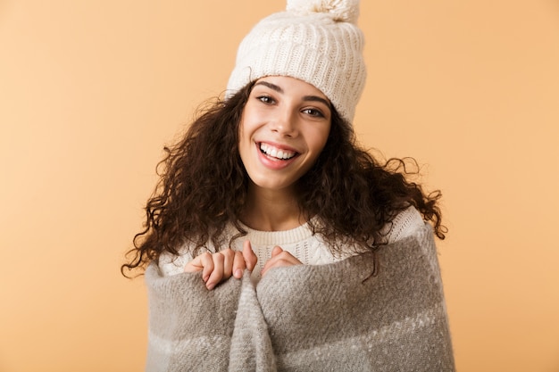 Fröhliche junge Frau, die Winterschal trägt, der lokal über beige Wand steht