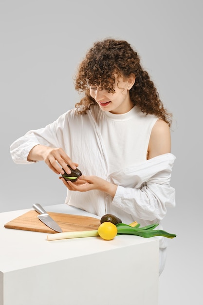 Fröhliche junge Frau dreht frisches Avocado und öffnet es