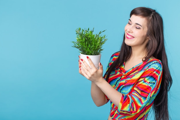 Fröhliche junge Frau hält einen Topf mit einer Pflanze, die gegen eine blaue Wand mit Copyspace aufwirft