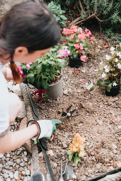 Fröhliche junge Frau in Handschuhen, die Gartengeräte zum Pflanzen von Blumen auf dem Hinterhof verwendet, lässig