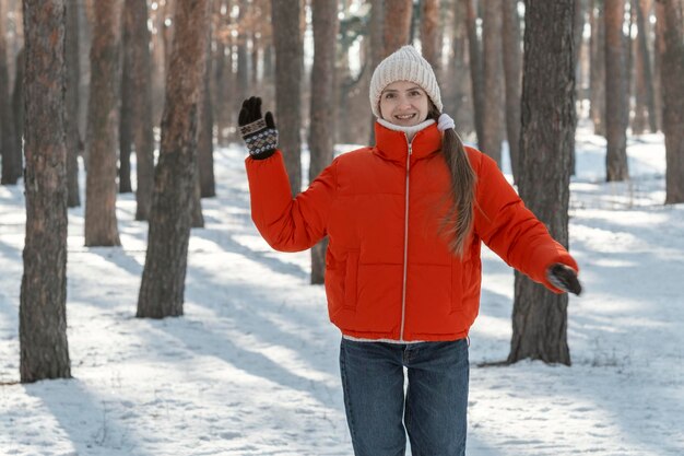 Fröhliche junge Frau in roter Jacke und Strickmütze freut sich an sonnigen Tagen Porträt eines Mädchens im schneebedeckten Winterwald