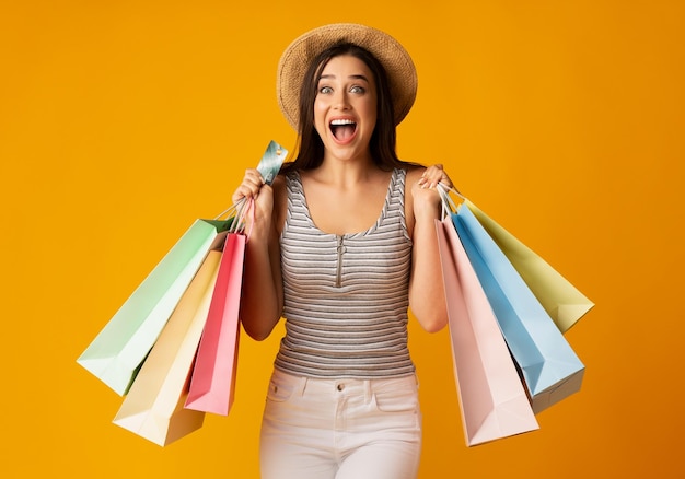 Fröhliche junge Frau mit bunten Einkaufstüten und Kreditkarte