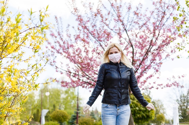 Fröhliche junge Frau mit Gesichtsmaske zum Schutz vor Viren, die an einem sonnigen Frühlingstag im Freien steht.