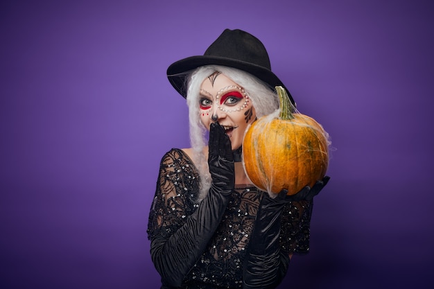 Fröhliche junge Frau mit Halloween-Make-up und Kürbis