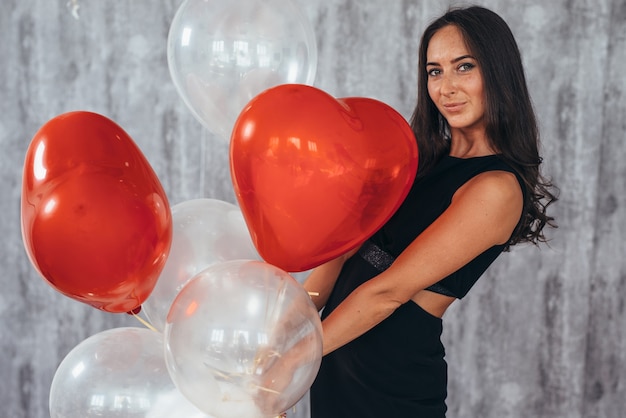 Fröhliche junge Frau mit Luftballons stehend und lächelnd.