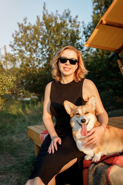 Fröhliche junge Frau mit walisischem Corgi Pembroke-Hund, die sich am Sommertag beim Glamping entspannt Luxus-Campingzelt für Erholung im Freien und Erholung Lifestyle-Konzept