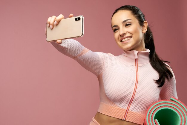 Fröhliche junge Frau mit Yogamatte macht Selfie