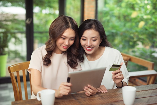 Fröhliche junge Frauen mit digitalem Tablet-Shopping online mit Kreditkarte im Café