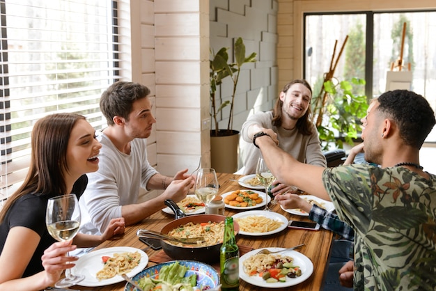 Fröhliche junge Freunde essen und haben Spaß am Tisch