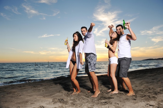 Fröhliche junge Freundesgruppe hat Spaß und feiert beim Springen und Laufen am Strand bei Sonnenuntergang